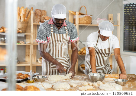 Two male bakers cutting dough and rolling it out Two male bakers cutting dough and rolling it out 120809681
