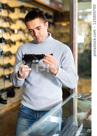Man with handgun at counter in weapon shop Man with handgun at counter in weapon shop 120809700