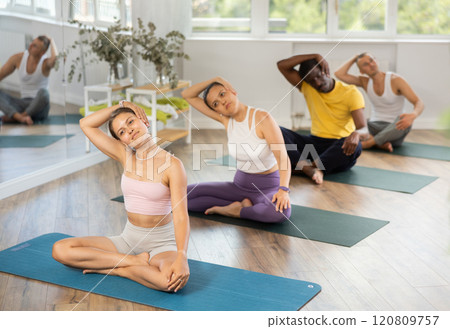Young woman coach and students perform variation of lotus asana during training in studio 120809757