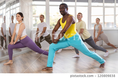 Active men and women dancing synchronous group choreography in dance hall. International group of dancers Active men and women dancing synchronous group choreography in dance hall. International group of dancers 120809838