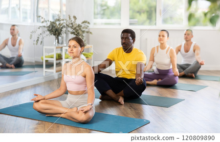 Young woman coach and students perform variation of lotus asana during training in studio 120809890