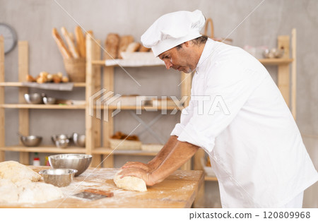 Adult male baker kneading dough on table Adult male baker kneading dough on table 120809968