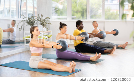 Students sitting on mat, holding fitball in outstretched hands, raising and lowering hands with ball 120810003