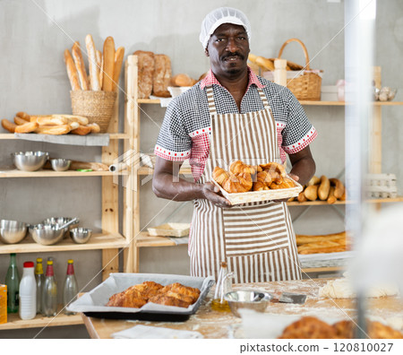 Happy male chef showing off croissants in his bakery Happy male chef showing off croissants in his bakery 120810027