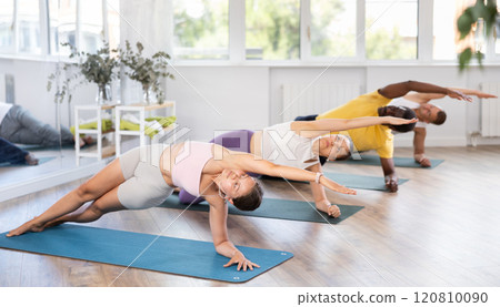 Young woman coach and students perform Vasishthasana during training in studio Young woman coach and students perform Vasishthasana during training in studio 120810090