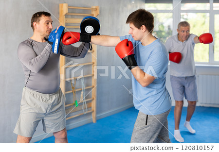 Boxing training - young guy masters boxing strikes on trainer punch mitts during training 120810157