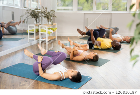 Asian woman performing Pawanmuktasana at group yoga session Asian woman performing Pawanmuktasana at group yoga session 120810187