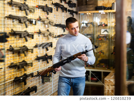 Man selecting assault rifle in air weapon shop Man selecting assault rifle in air weapon shop 120810239
