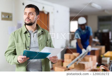 Focused man standing at indoors building site, reading document Focused man standing at indoors building site, reading document 120810272