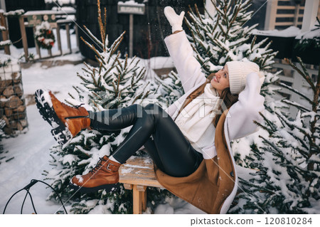 Smiling woman enjoying winter by sitting in the snow surrounded by pine trees Smiling woman enjoying winter by sitting in the snow surrounded by pine trees 120810284