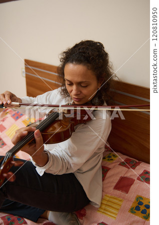 Woman practicing violin in bedroom for a calming musical session Woman practicing violin in bedroom for a calming musical session 120810950