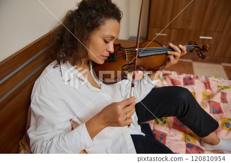 Woman playing violin while sitting on a colorful quilted bed 120810954