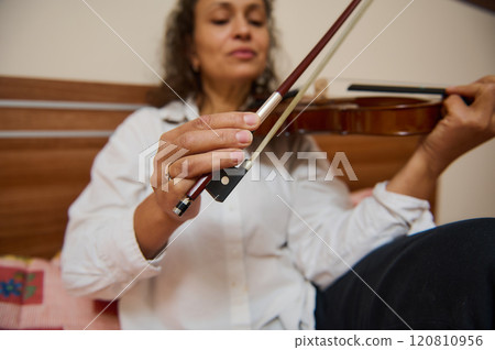 Woman plays violin indoors, focusing on bow and strings technique 120810956