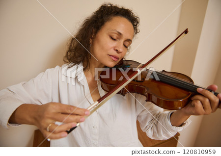 Woman peacefully playing violin with eyes closed in calm setting 120810959