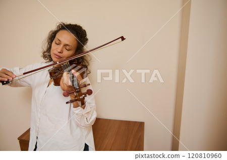 Serene woman playing violin with eyes closed in peaceful moment 120810960