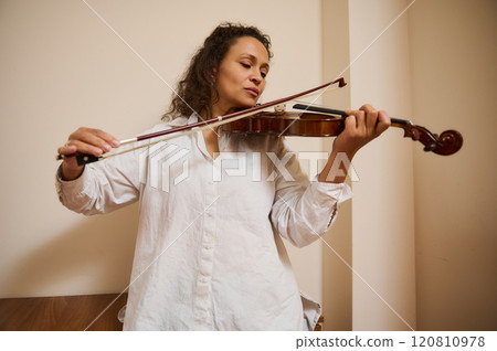 Woman passionately plays violin in relaxed indoor setting Woman passionately plays violin in relaxed indoor setting 120810978
