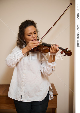 Woman practicing violin passionately in a cozy indoor setting 120810982
