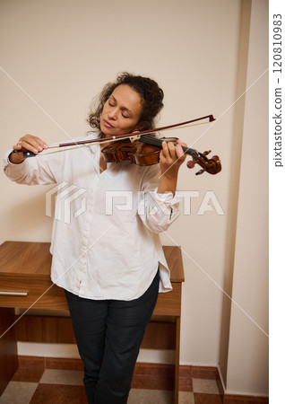 Woman playing violin with closed eyes in serene indoor setting Woman playing violin with closed eyes in serene indoor setting 120810983