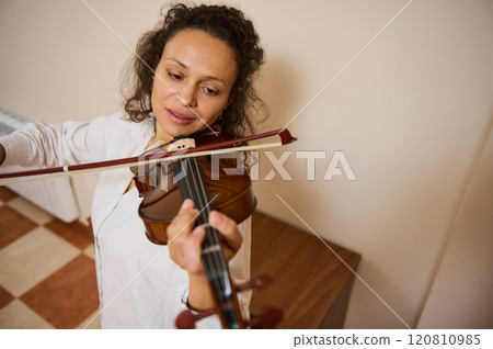 Woman in white shirt playing a violin passionately in a cozy room Woman in white shirt playing a violin passionately in a cozy room 120810985
