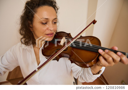 Woman playing violin indoors, focused on music in a serene setting Woman playing violin indoors, focused on music in a serene setting 120810986