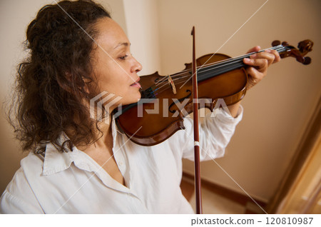Woman playing a violin in a bright room with concentration 120810987