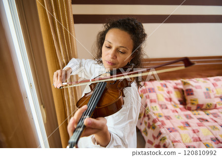 Woman playing violin gracefully in a cozy bedroom setting 120810992