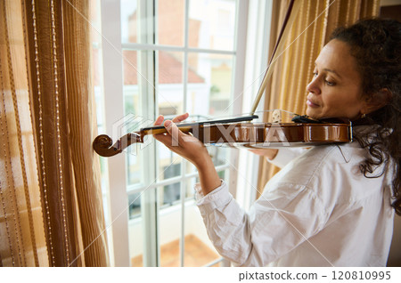 Woman playing a violin by a sunlit window in serene setting 120810995
