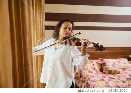 Relaxed woman playing violin in cozy bedroom setting Relaxed woman playing violin in cozy bedroom setting 120811011