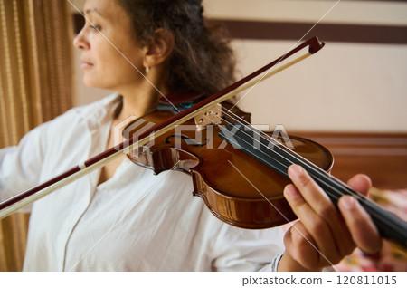 Close-up of woman playing violin in warmly lit room Close-up of woman playing violin in warmly lit room 120811015
