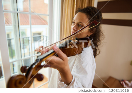 Young musician practicing violin near a sunlit window indoors Young musician practicing violin near a sunlit window indoors 120811016