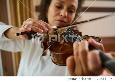 Close-up of woman playing violin, focusing on hand and strings detail Close-up of woman playing violin, focusing on hand and strings detail 120811026