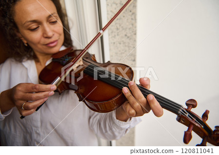 Woman playing the violin with focus and elegance by a window 120811041