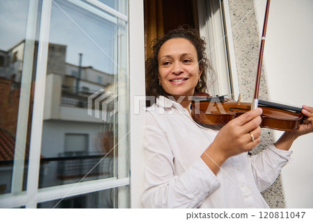 Woman joyfully playing violin near a window with urban background 120811047