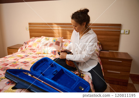Woman preparing violin on a bed with a colorful quilt cover 120811195