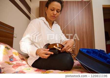Woman preparing violin for practice in cozy bedroom setting Woman preparing violin for practice in cozy bedroom setting 120811196