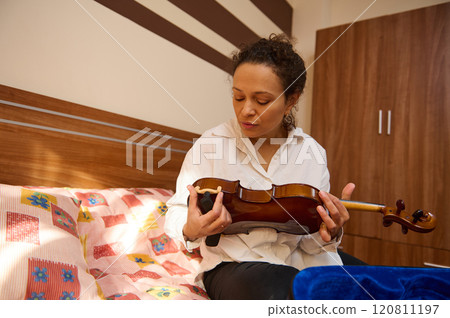 Woman in white shirt carefully inspecting a violin in bedroom setting Woman in white shirt carefully inspecting a violin in bedroom setting 120811197