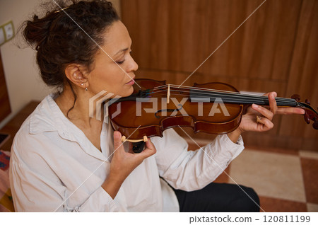 Woman playing the violin with focus and passion in a warm room Woman playing the violin with focus and passion in a warm room 120811199