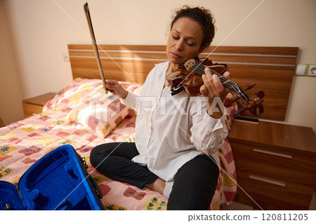 Woman playing violin on bed in cozy bedroom setting Woman playing violin on bed in cozy bedroom setting 120811205