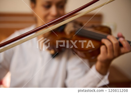 Close-up of hands playing a violin with focus on the strings and bow Close-up of hands playing a violin with focus on the strings and bow 120811208