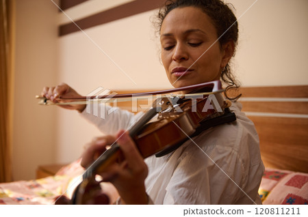 Woman gracefully playing the violin in a serene bedroom setting Woman gracefully playing the violin in a serene bedroom setting 120811211
