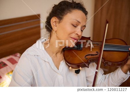 Woman peacefully enjoying music while playing the violin at home 120811227