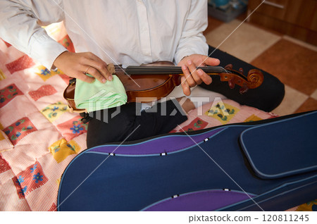 Person carefully cleaning a violin while sitting on a colorful bed 120811245