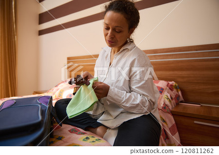 Woman preparing violin at home, seated on colorful bedspread Woman preparing violin at home, seated on colorful bedspread 120811262