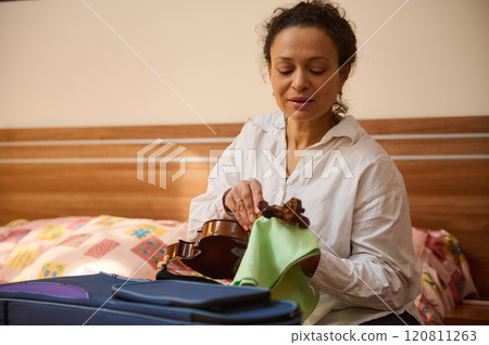Woman preparing violin in cozy bedroom setting for practice session Woman preparing violin in cozy bedroom setting for practice session 120811263