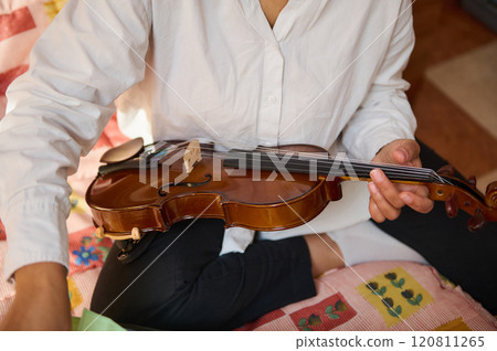 Person practicing violin while sitting cross-legged on a colorful quilt Person practicing violin while sitting cross-legged on a colorful quilt 120811265