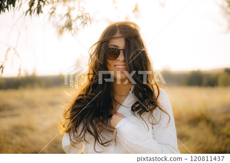 A woman wearing sunglasses. She is smiling and she is enjoying her walk. A woman wearing sunglasses. She is smiling and she is enjoying her walk. 120811437