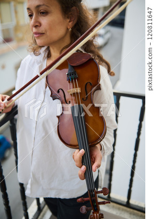Woman playing violin outdoors on a balcony during the day 120811647