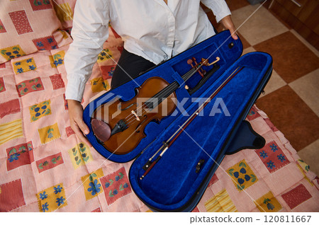 Person opening violin case on colorful patterned bed in room 120811667