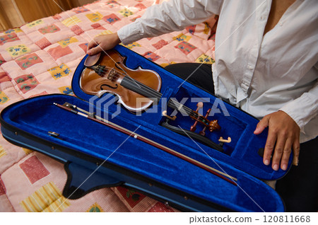 Person opening violin case on bed with colorful quilt cover 120811668