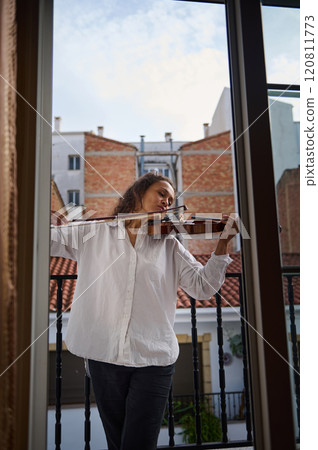 Woman playing violin on a balcony with cityscape background Woman playing violin on a balcony with cityscape background 120811773
